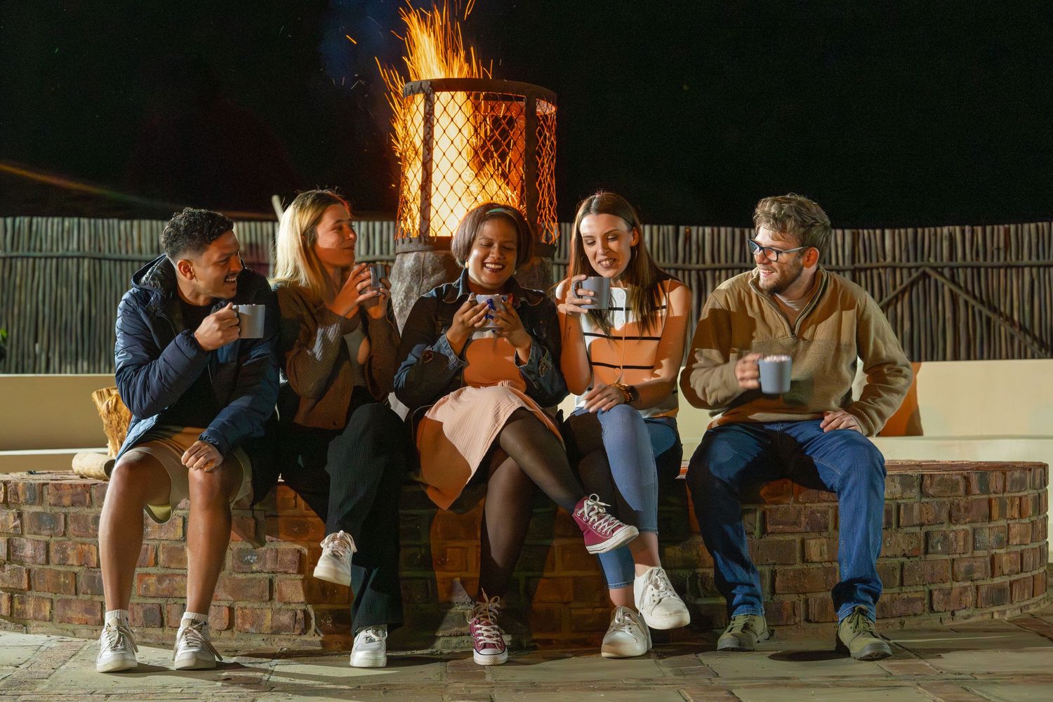 Young adults enjoying a hot chocolate in front of a campfire