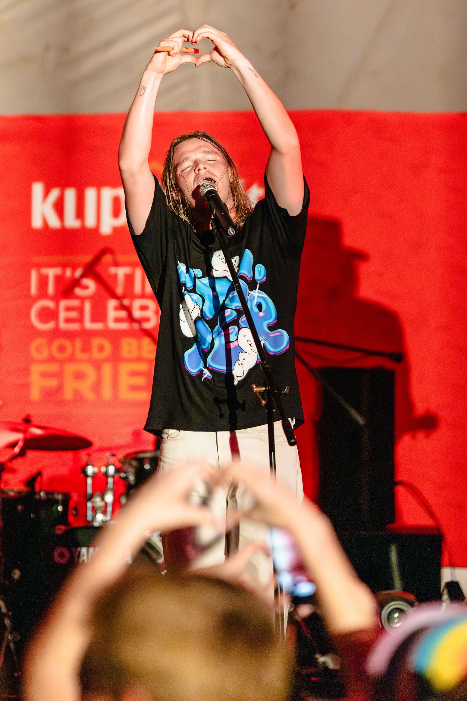 Concert performers on stage with red backdrop and dramatic lighting during a live show.