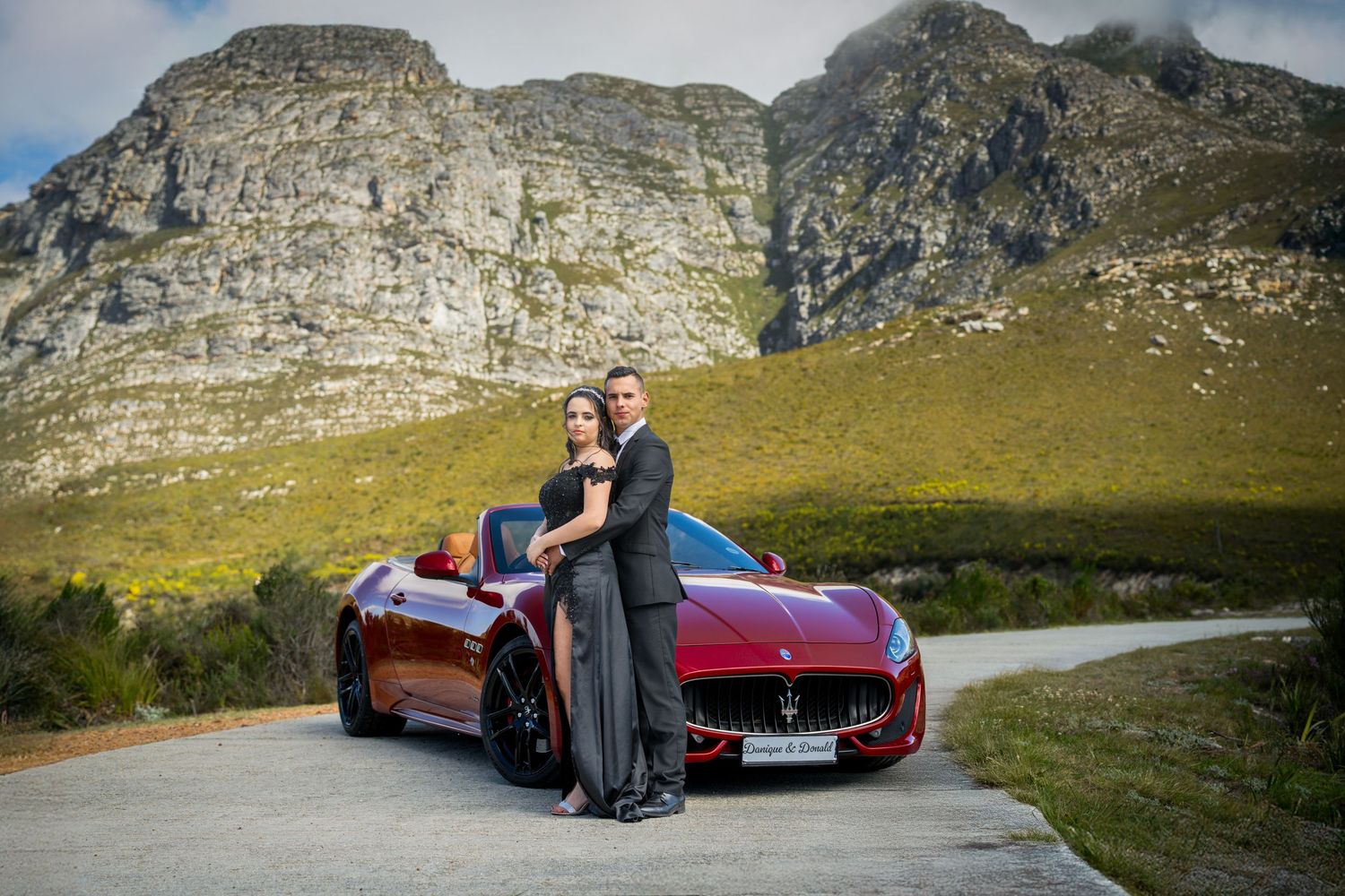 A red sports car parked on a mountain road with dramatic rocky cliffs in the background.