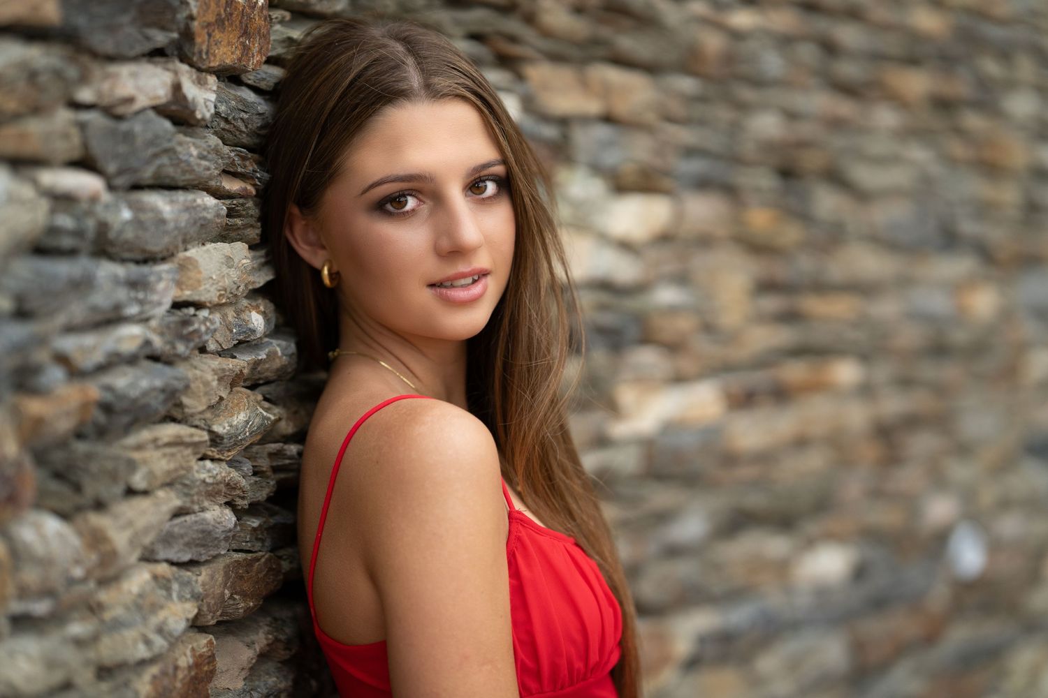 Model in a red dress leaning against a wall, looking towards the camera.