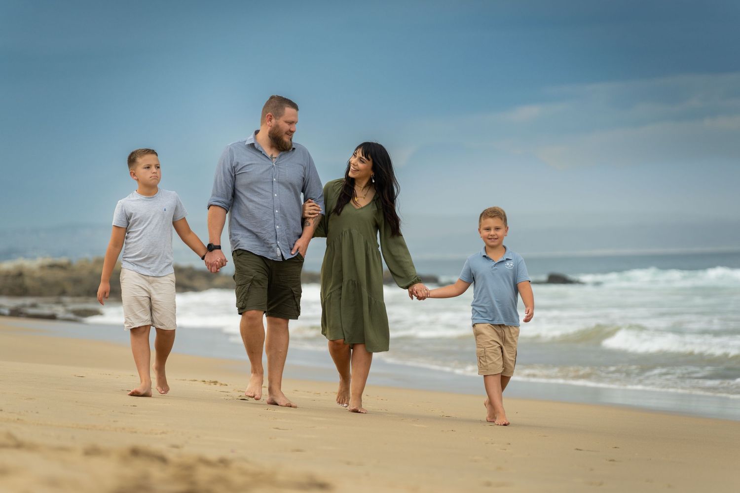 Family walking together along a scenic beach shoreline with waves crashing.