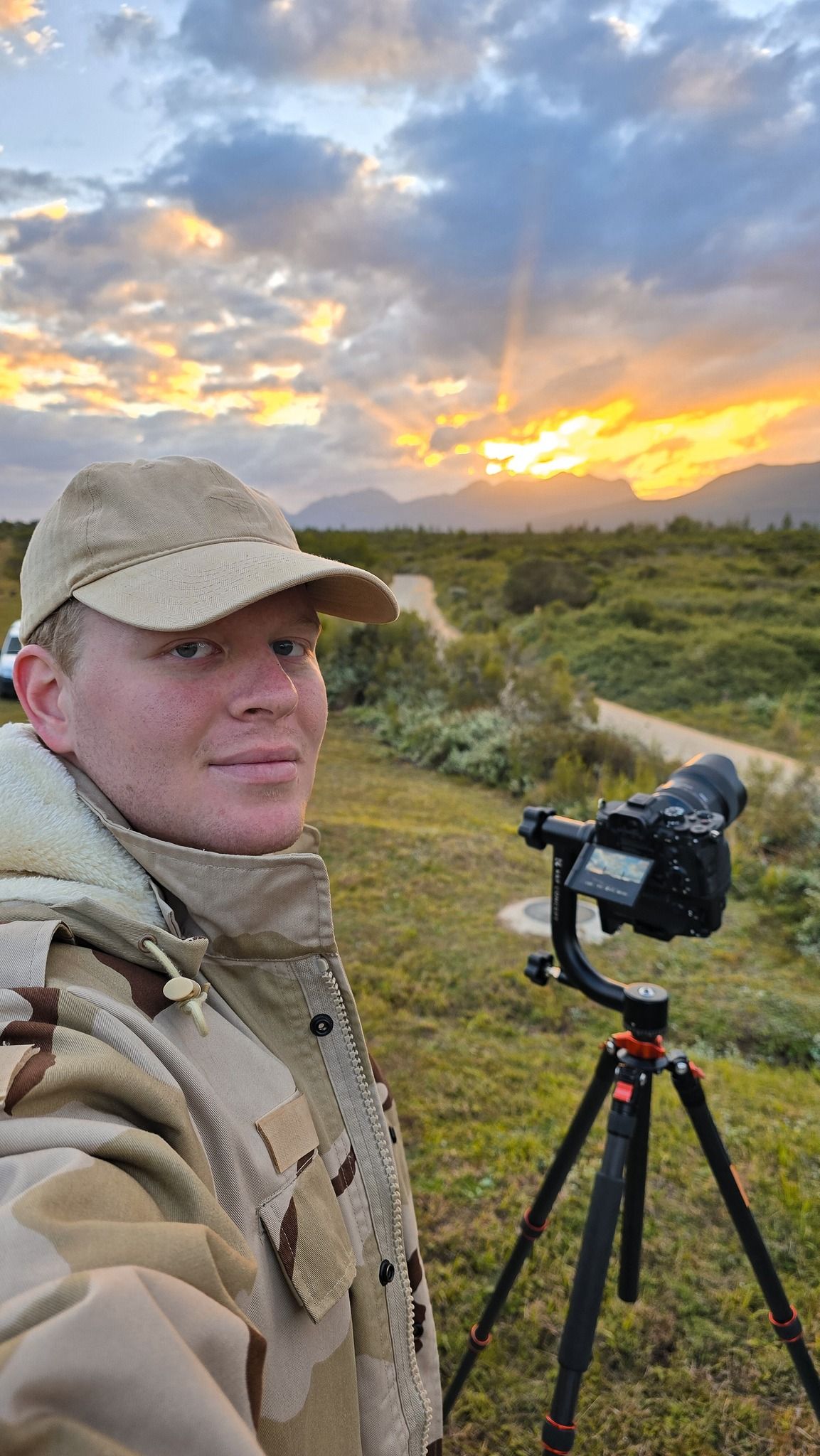Photographer with camera equipment capturing sunset landscape in outdoor wilderness setting.