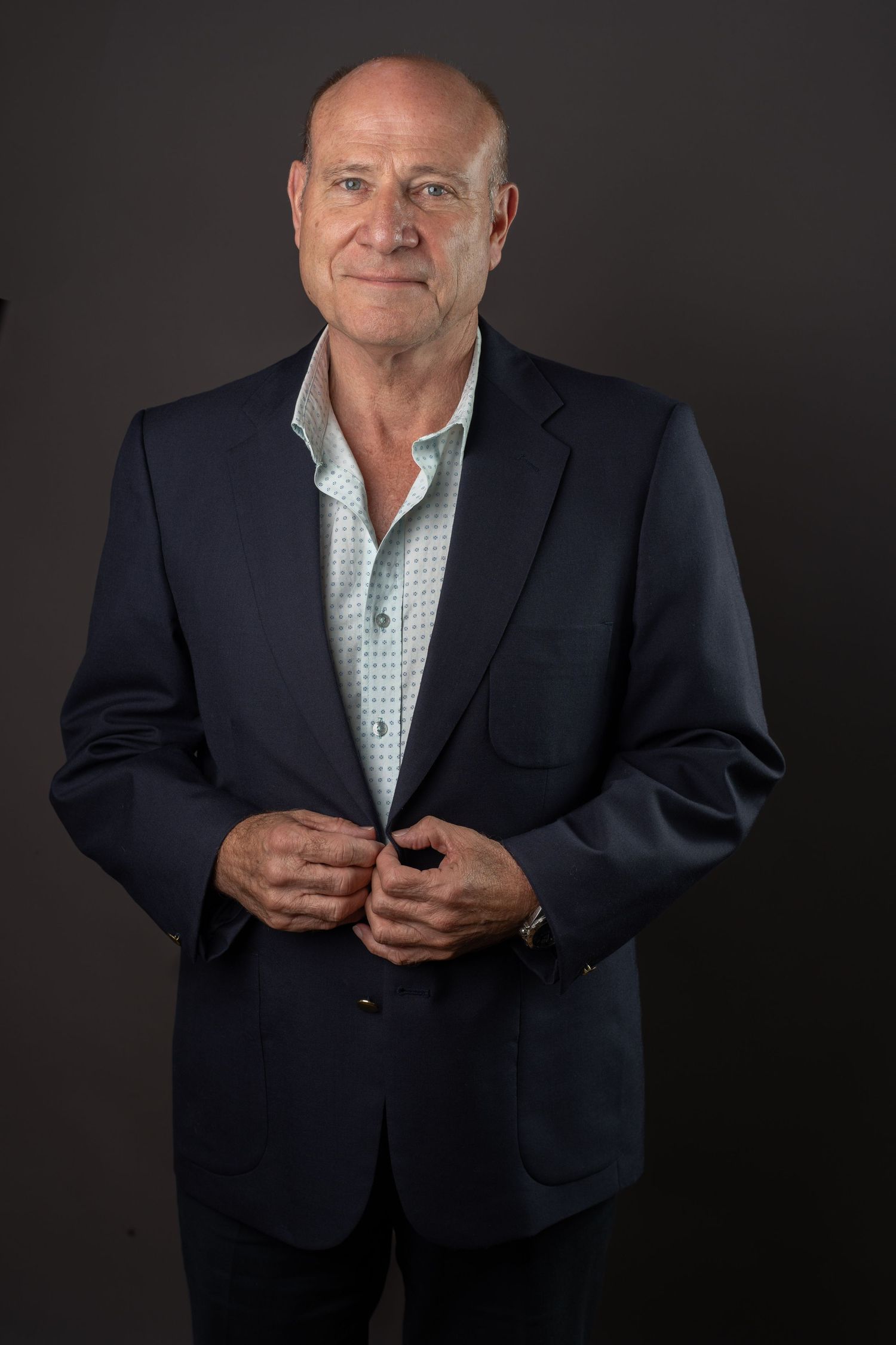 Professional studio portrait against dark background showing navy suit and white shirt.