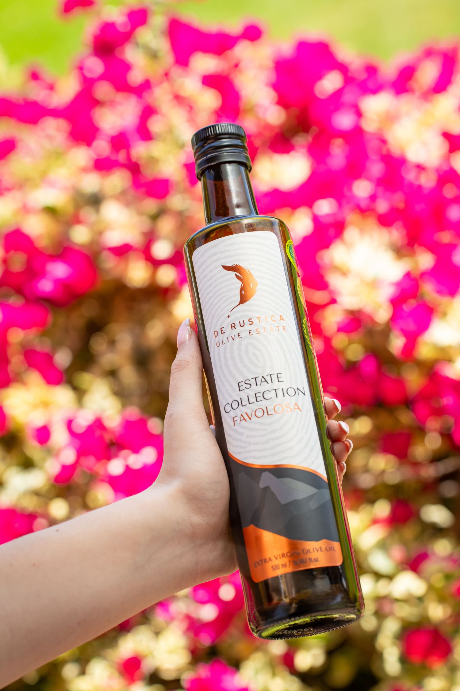Bottle of olive oil held by a models hand in front of pink roses