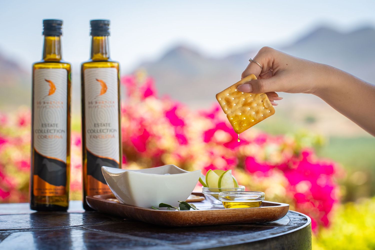 Wine bottles and appetizers arranged on an outdoor table with vibrant pink flowers in the background.