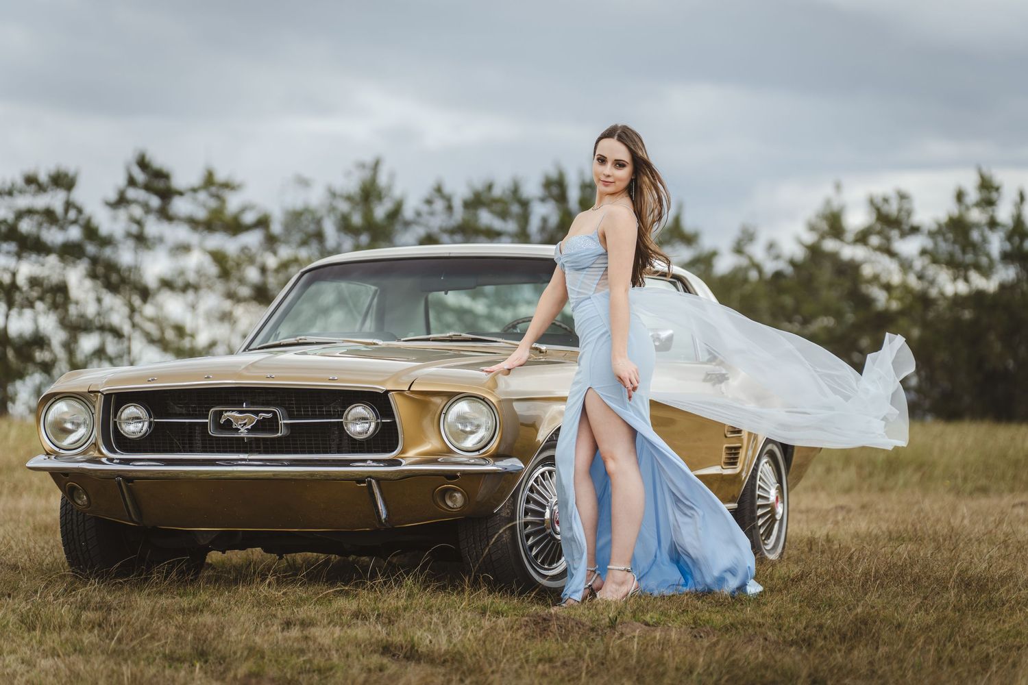 Woman in a blue dress posing beside a vintage car in an open field