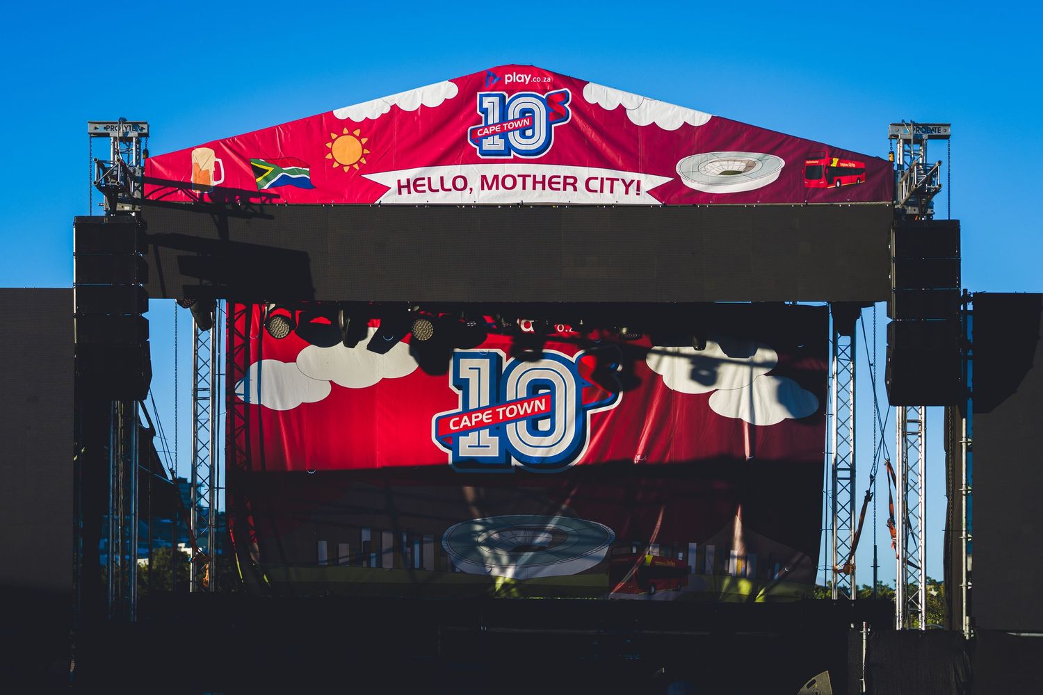 A vibrant red stage with 'Hello, Mother City!' banner celebrating Cape Town's 10th anniversary event under a clear blue sky.