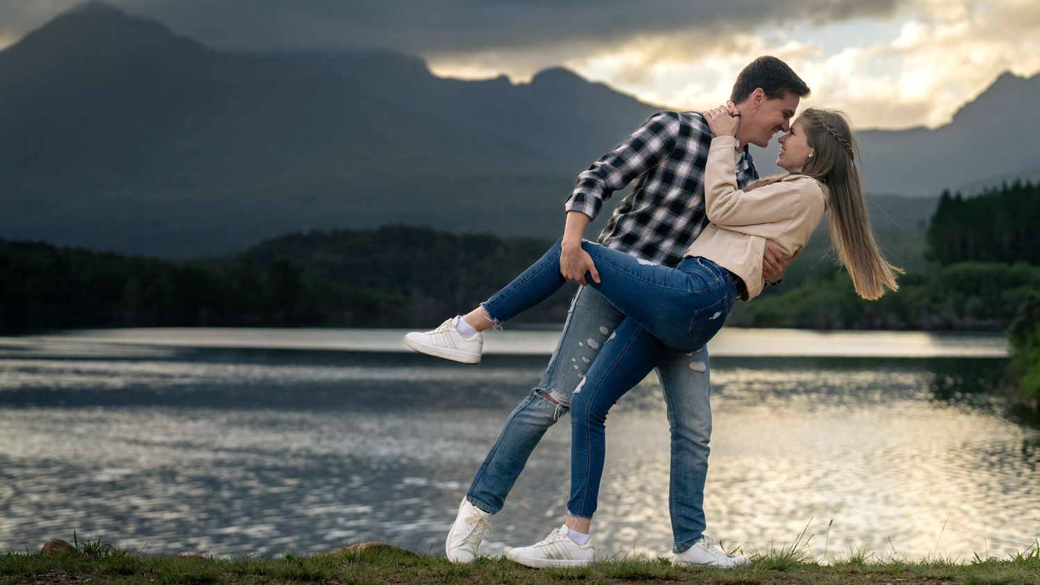 Couple embracing by a lake with mountains in the background at sunset
