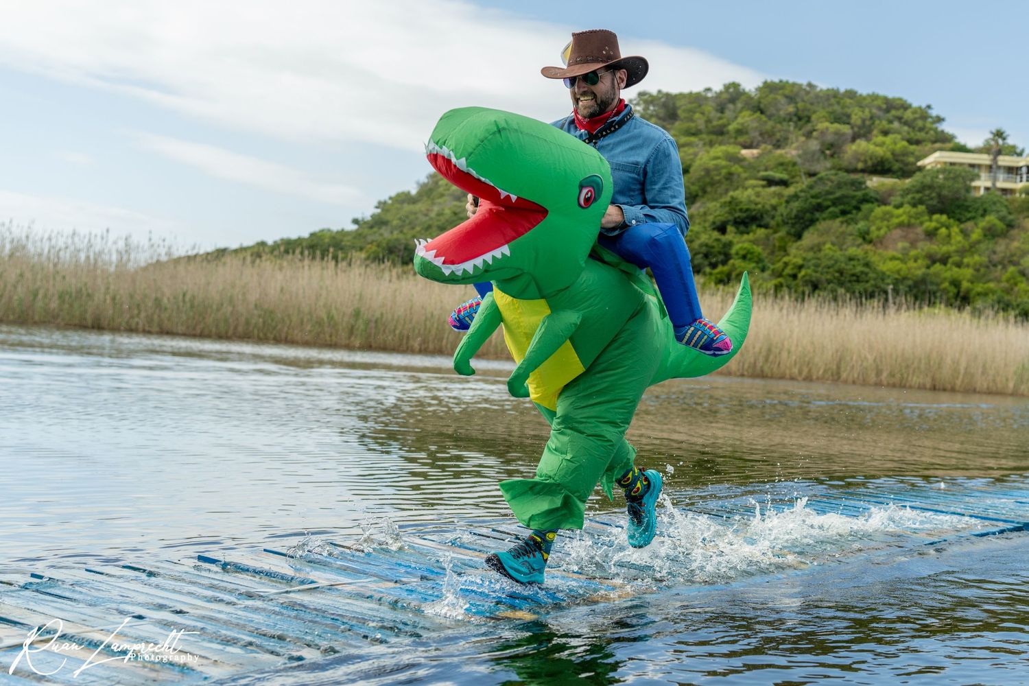 Man dressed as a Dinosaur running over a water bridge towards the finish line of a trail running event in Wilderness, Garden Route