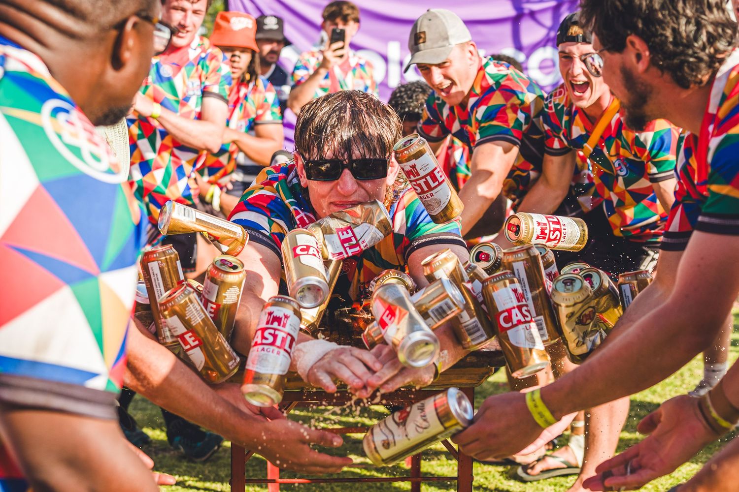 Festivalgoers in colorful jerseys pile up beer cans at an outdoor music festival event.