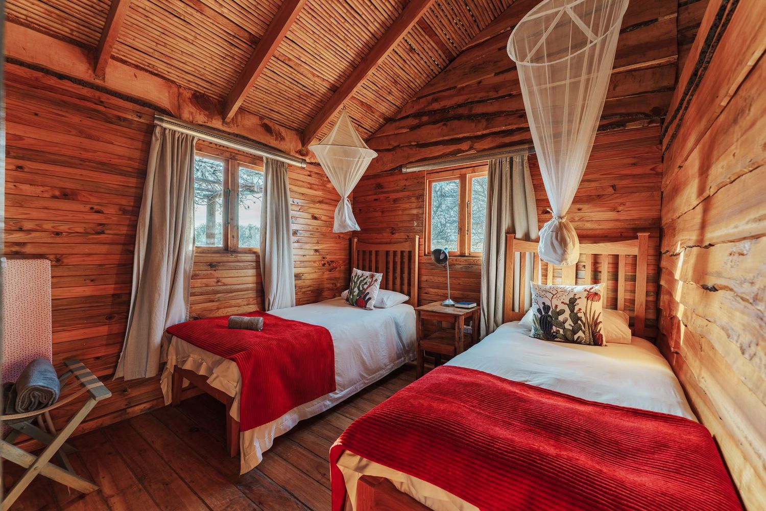Bedroom of a rustic wooden cabin with 2 single beds and mosquito nets