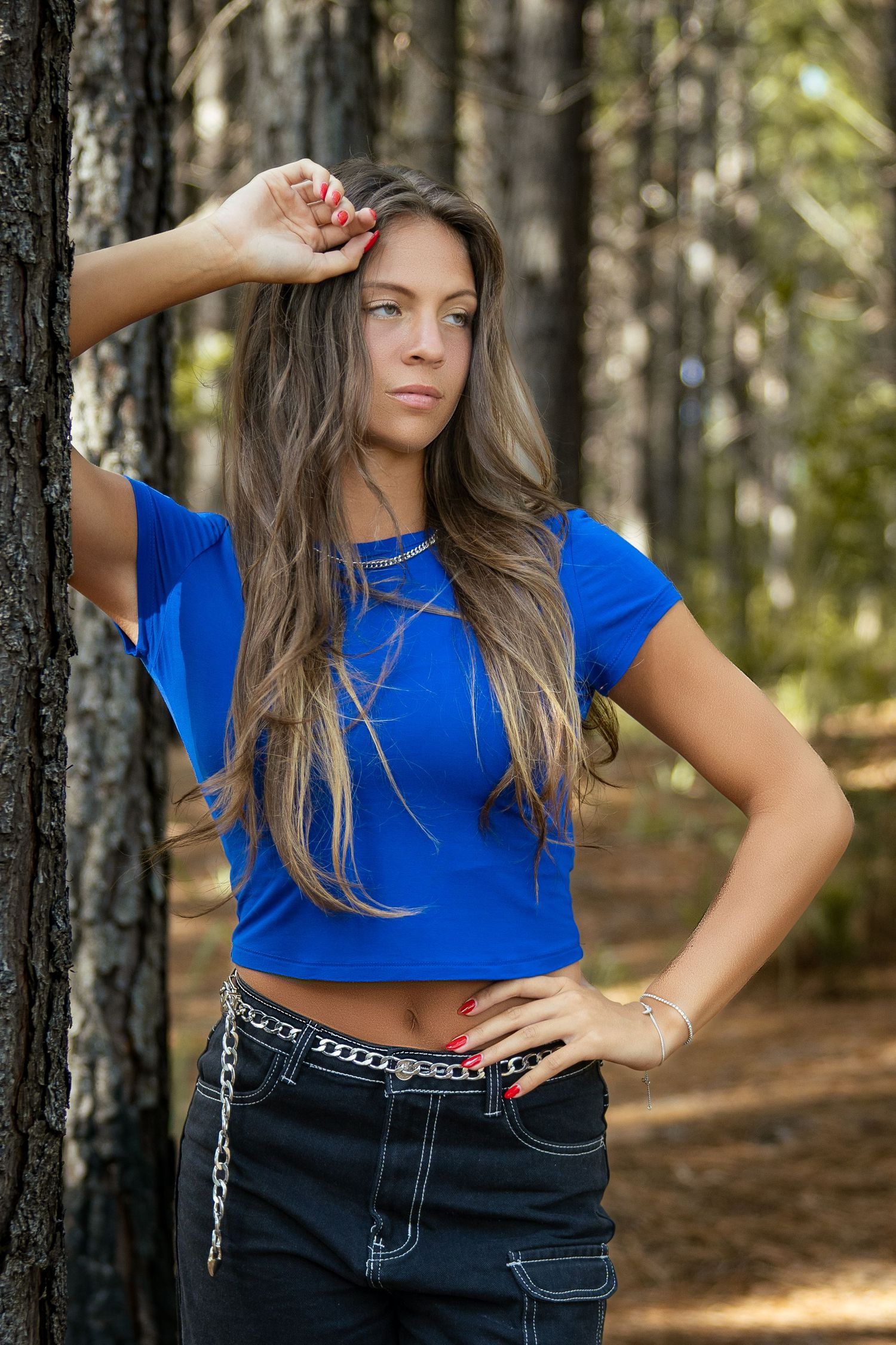 Woman posing against a tree wearing a blue top in a forest setting