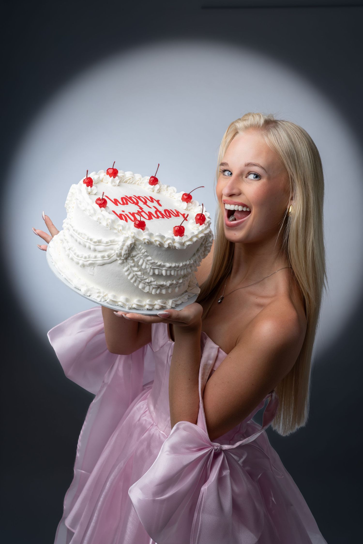 A festive birthday cake held up against a dark background with dramatic lighting.