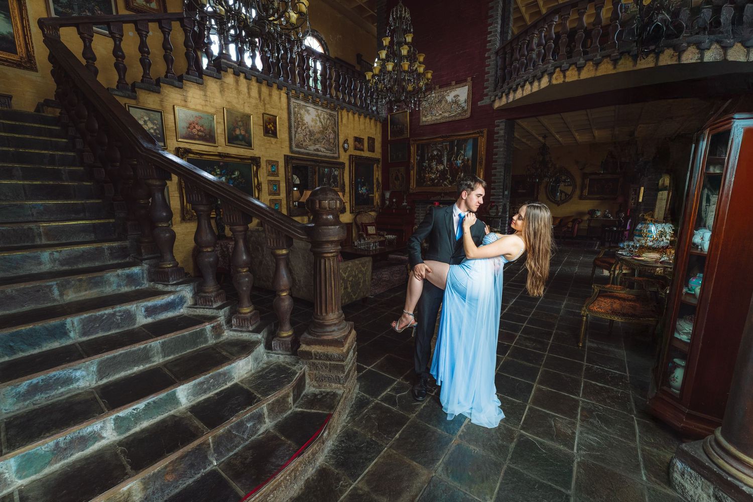 A couple poses in formal attire on an ornate wooden staircase in a historic building.
