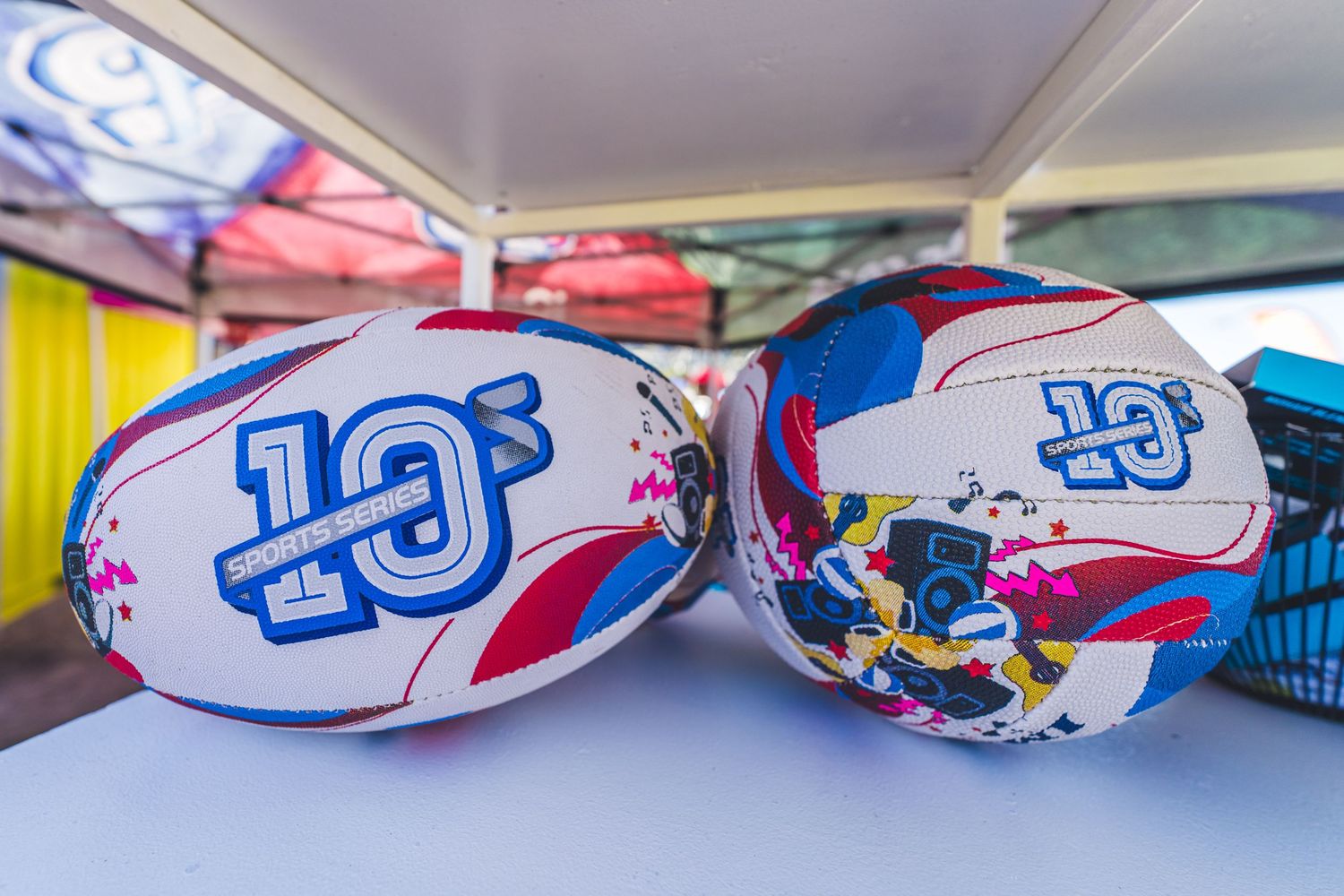 Two colorful rugby balls with the number 10s logo displayed on a white surface at a sporting event.