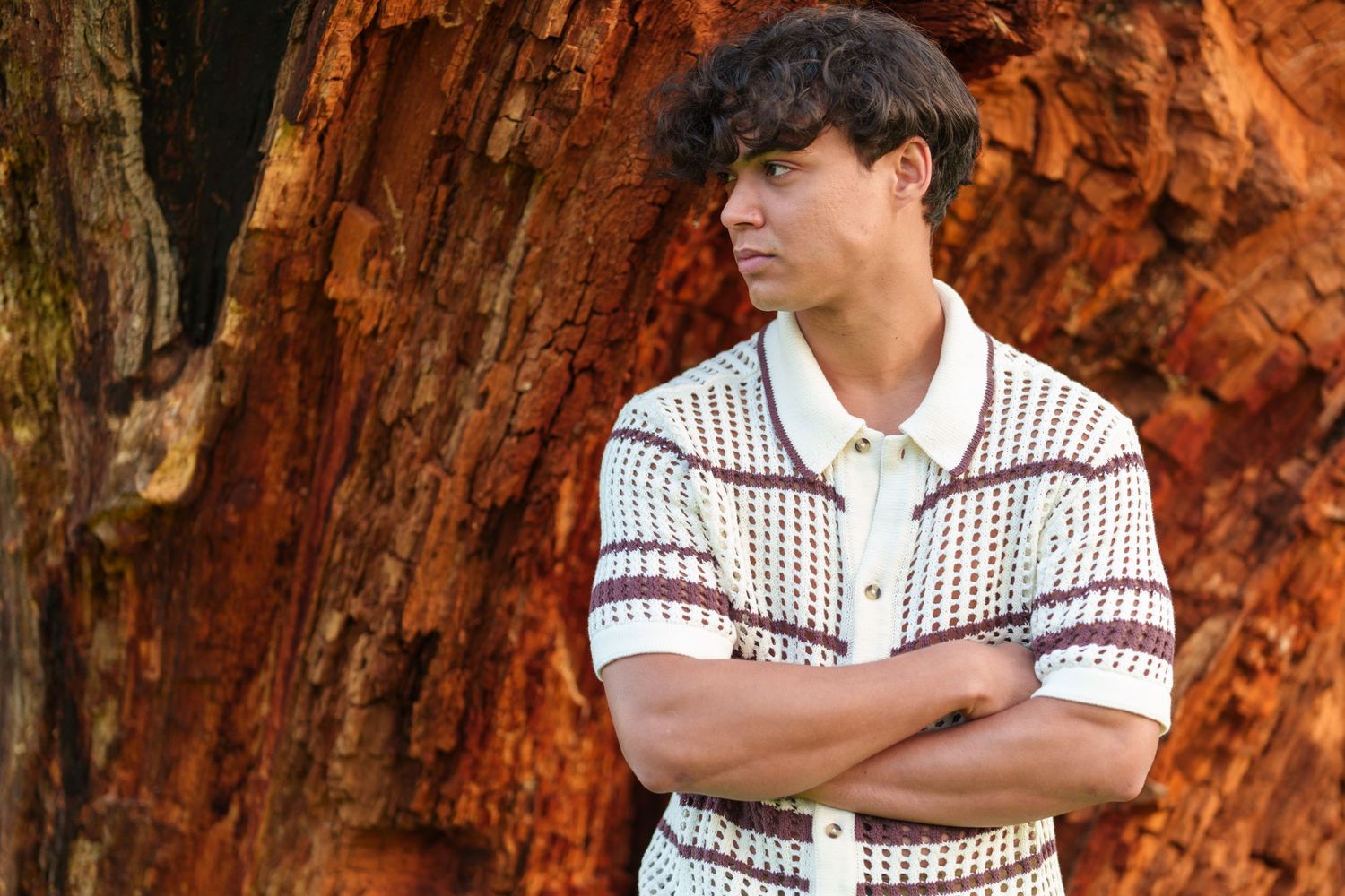 Young man posing against a textured tree trunk outdoors