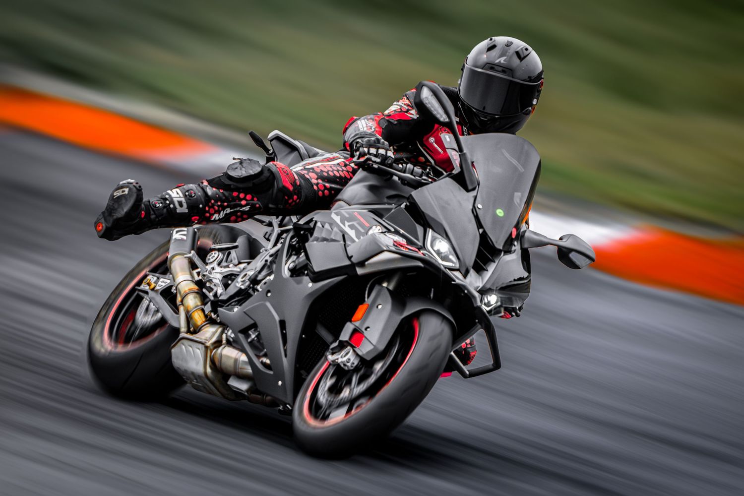 Rider in black and red gear racing a dark sport motorcycle on a track, captured with motion blur effect.