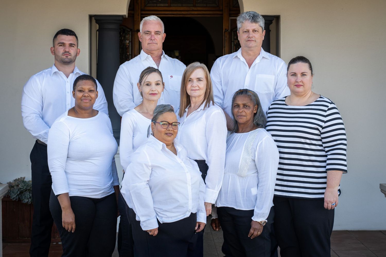 Professional group photo with people wearing coordinated white shirts and black attire.