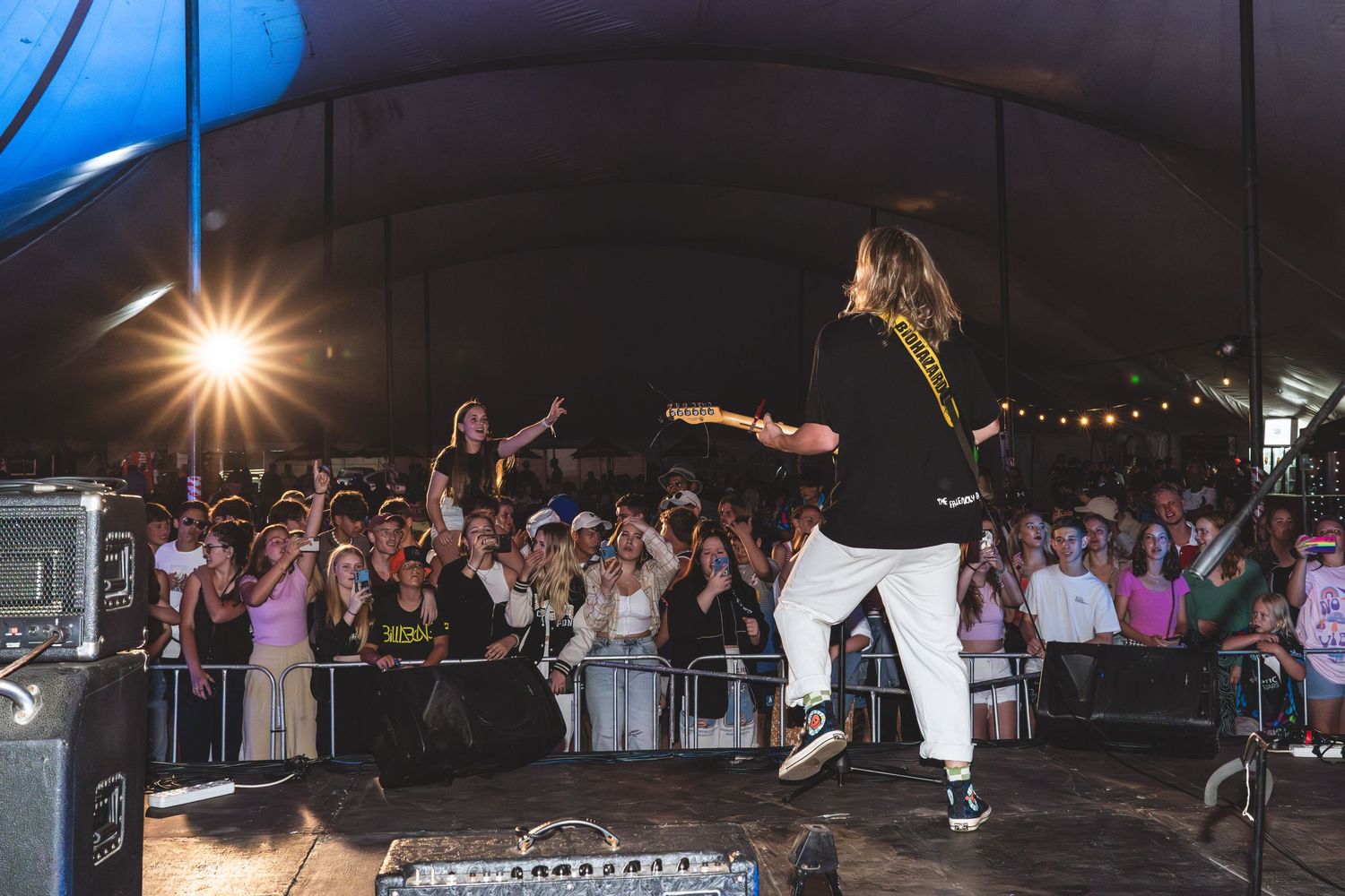 Energetic concert crowd enjoying a nighttime performance with stage lighting and hands in the air.
