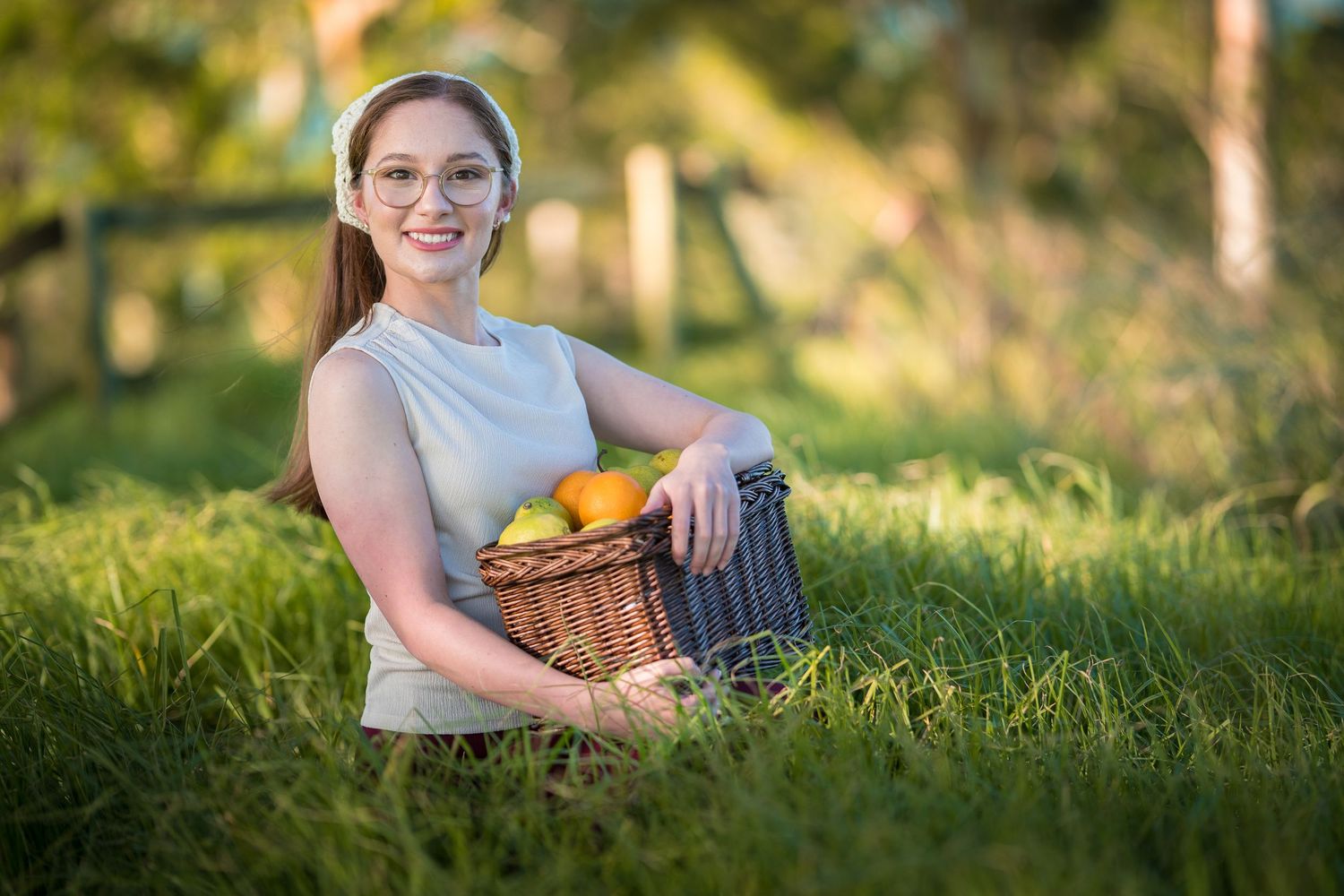 A person sits in lush green grass during golden hour while holding a ginger cat in their arms.