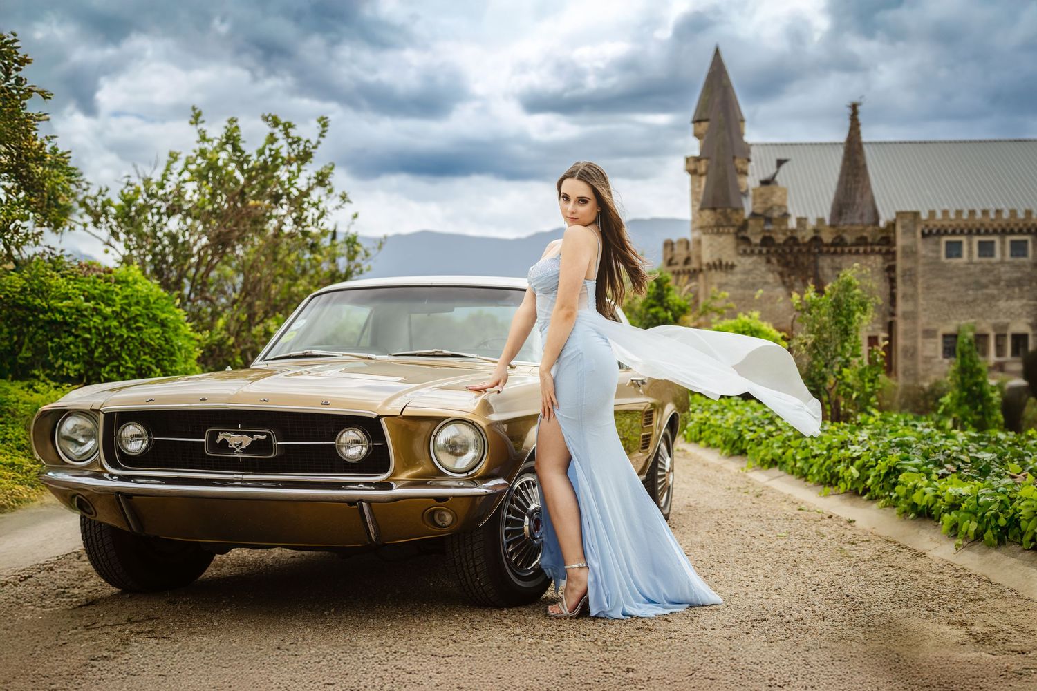 Woman in a blue dress posing next to a vintage car at a castle location