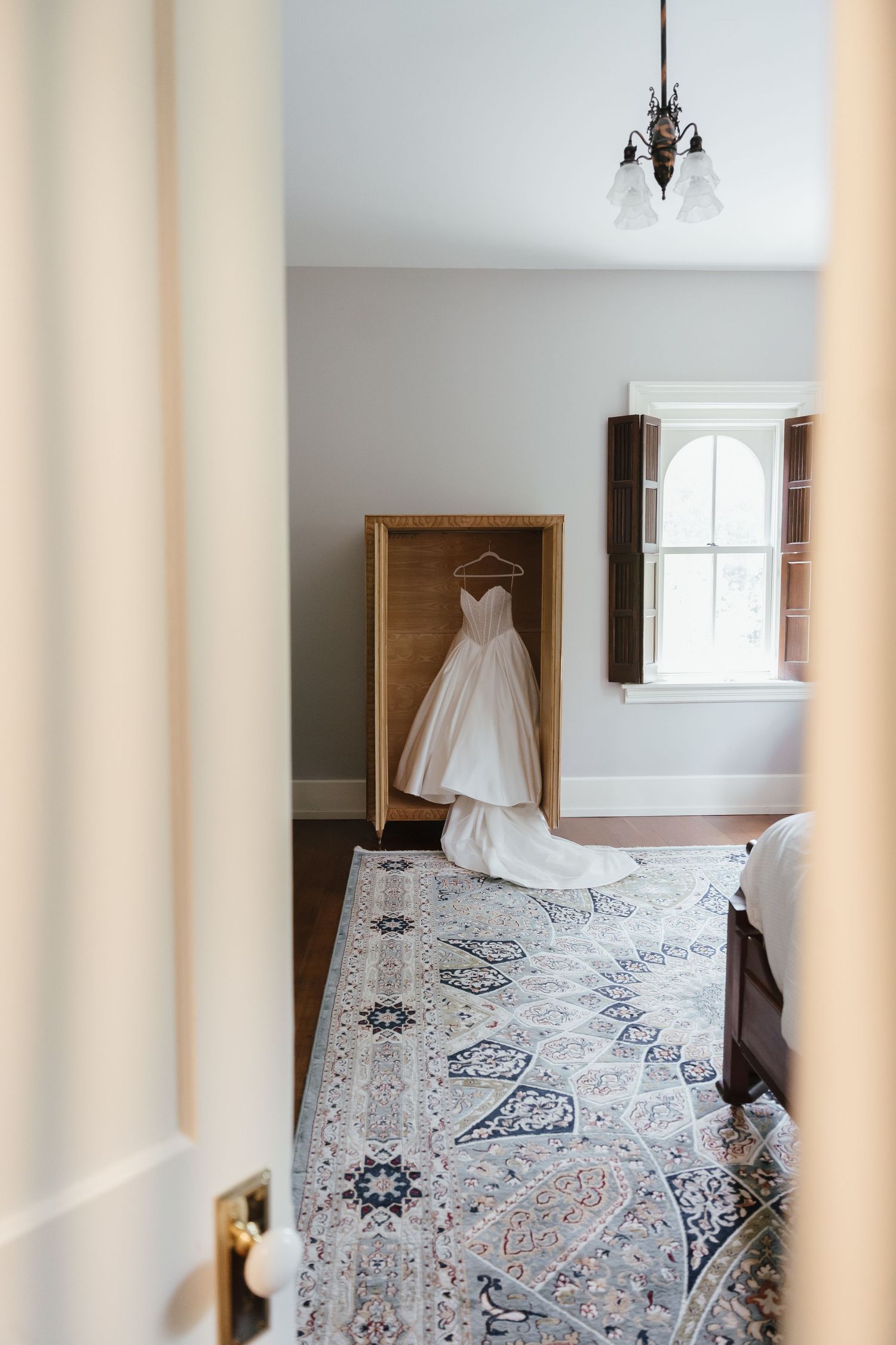 Elegant strapless wedding gown displayed on a wooden hanger in a charming vintage-style bridal suite.