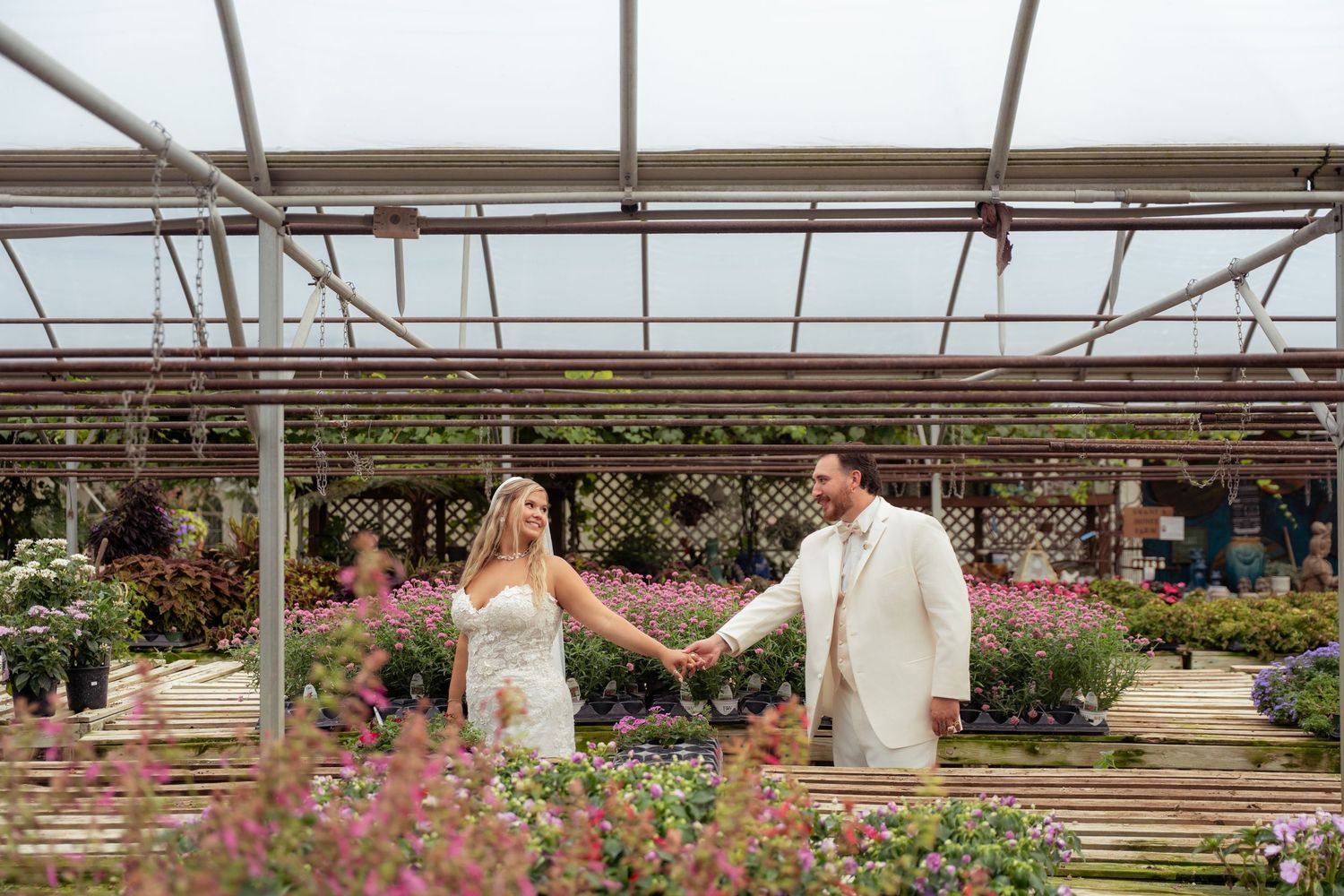 Bride and groom holding hands in a colorful flower greenhouse on wedding day.