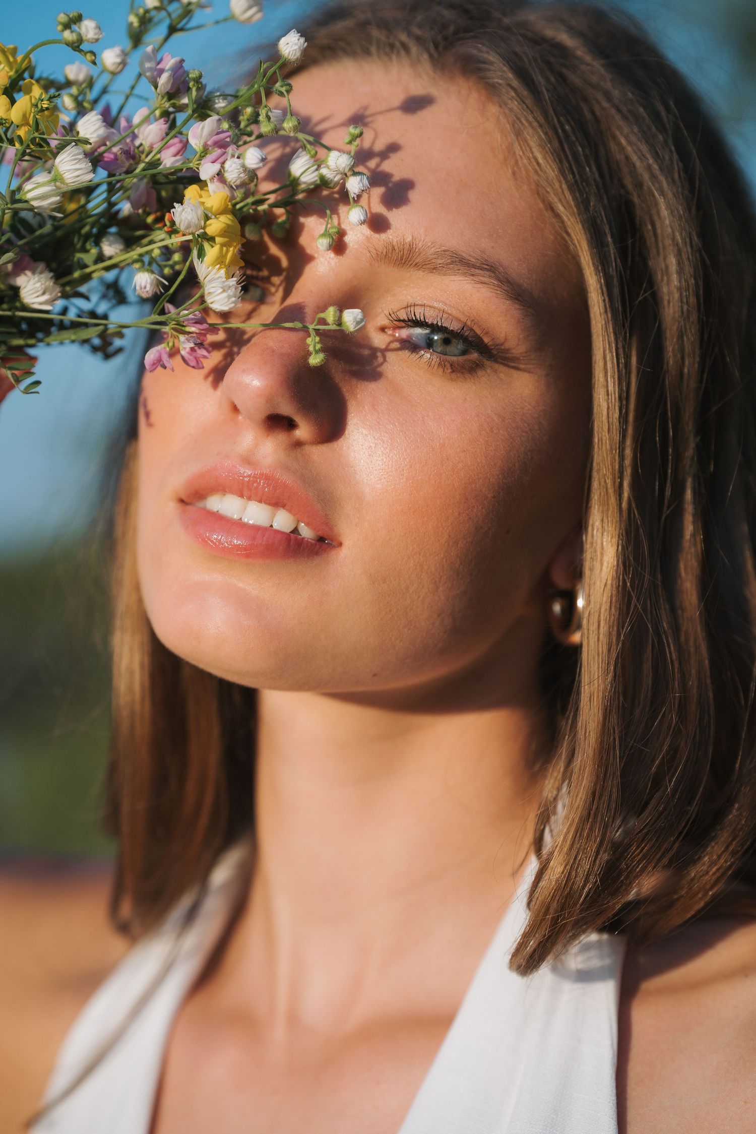 Close-up portrait of woman with wildflowers casting shadows across her face.