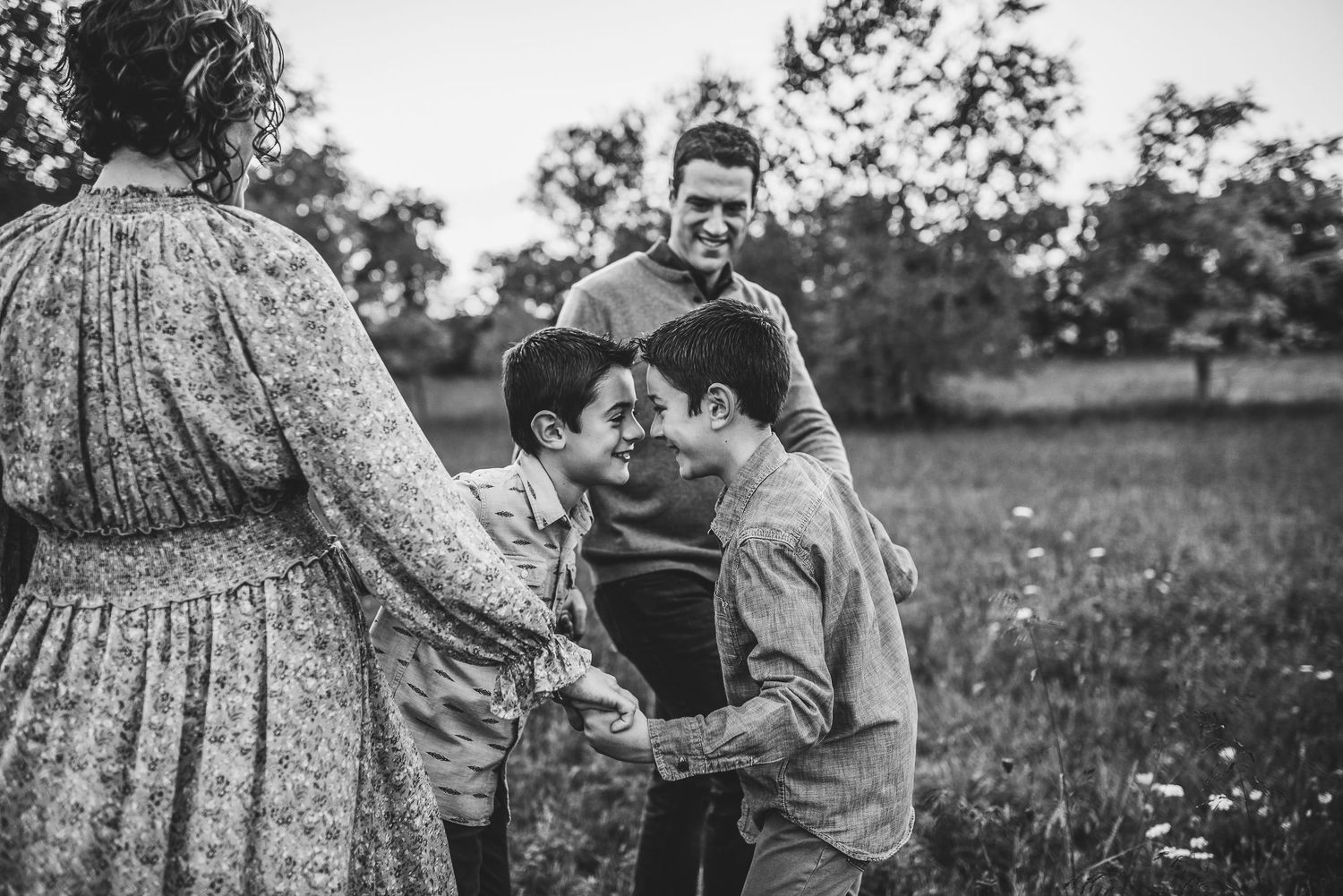 A black and white photo of two boys touching foreheads while parents smile in a flower field.