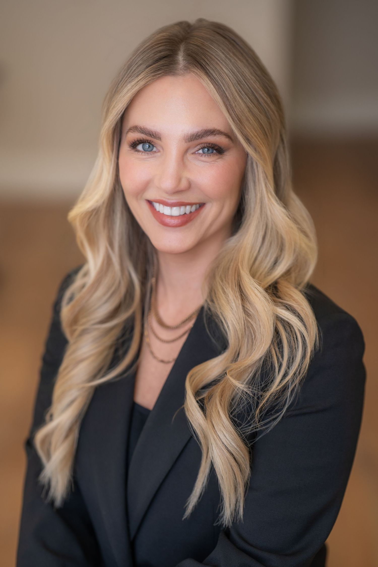 Professional blonde woman in black blazer smiling in corporate headshot portrait.