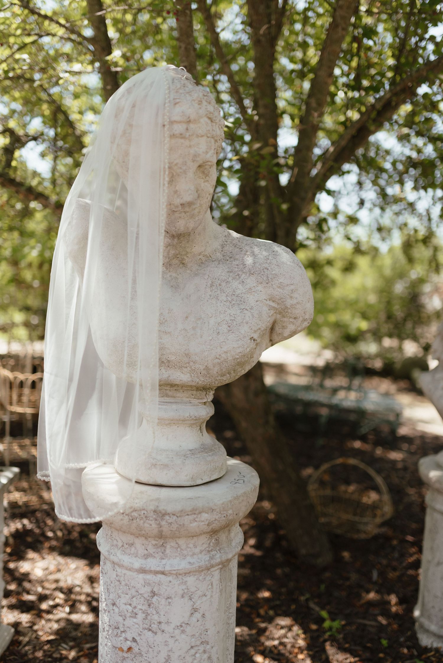 Stone bust sculpture adorned with a bridal veil in an outdoor garden setting.