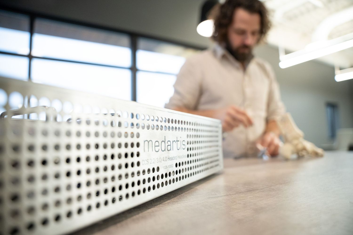 Man working at desk with white Medartis branded perforated metal device in foreground.