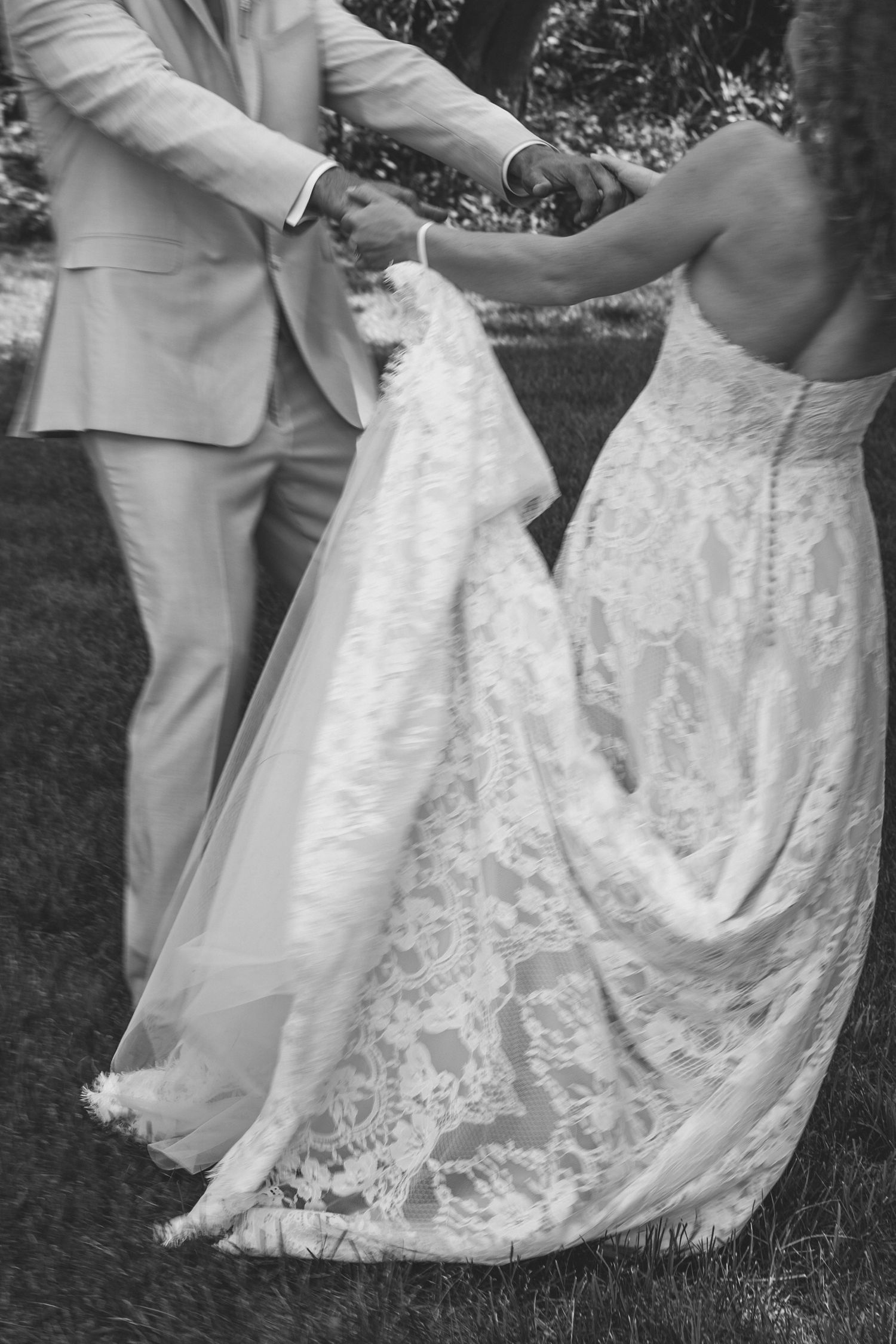 Black and white photo of bride and groom holding hands outdoors on wedding day.