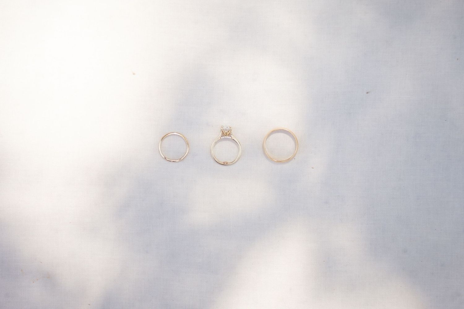 Three delicate gold rings arranged in a row on a light gray surface.