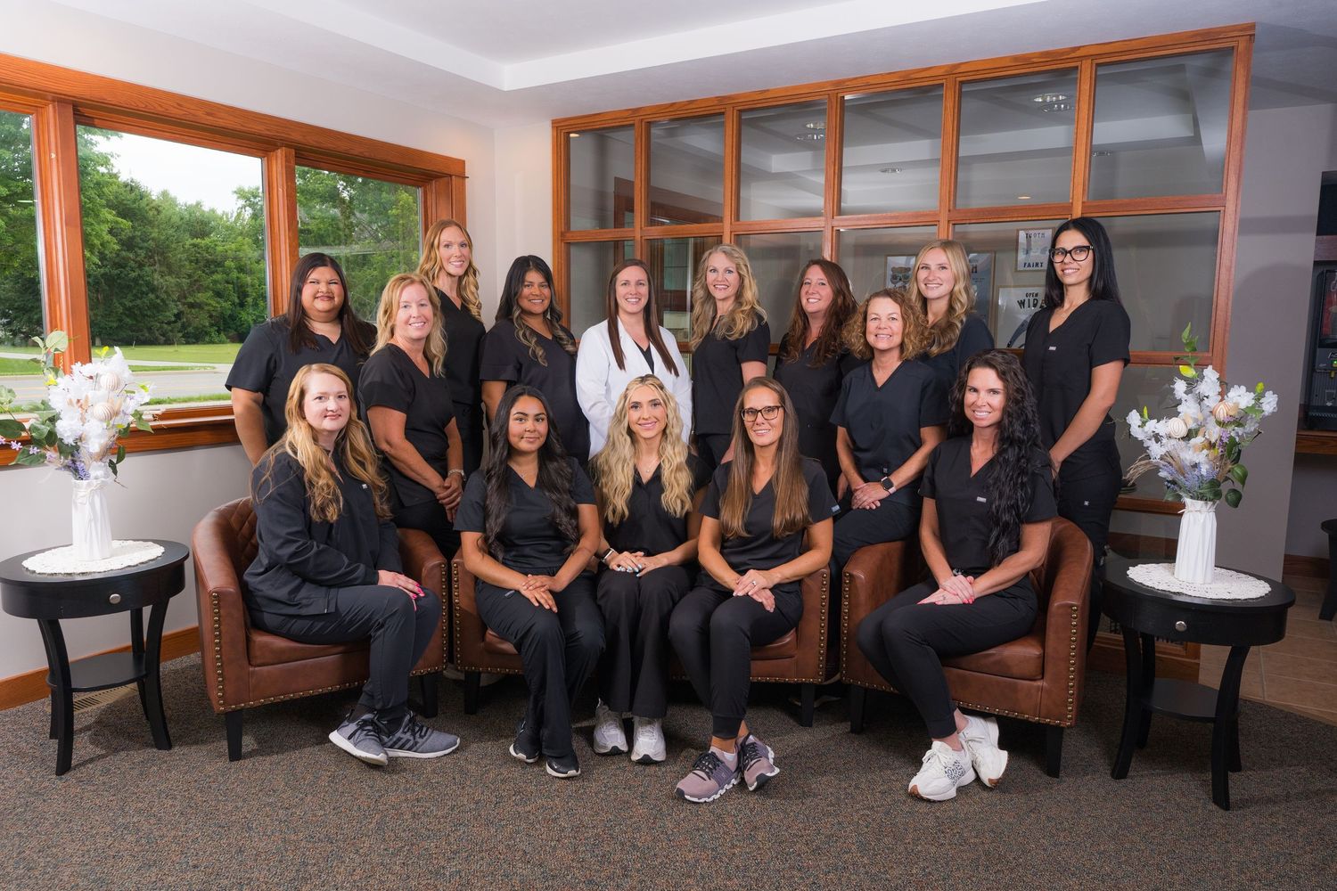 Group portrait of dental office team in black scrubs posing in waiting room.