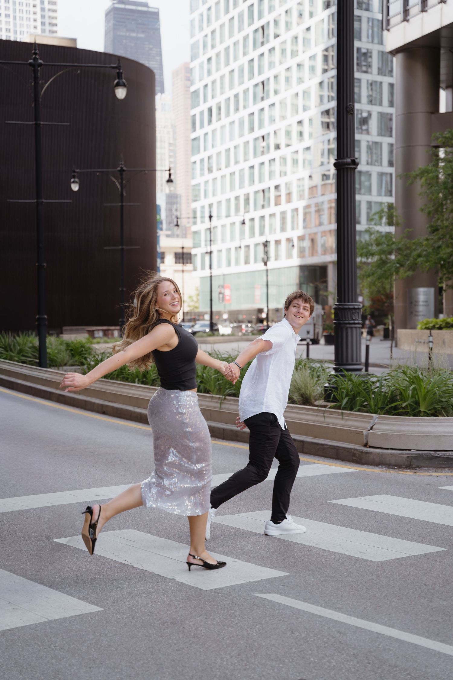 Happy couple holding hands while skipping across an urban crosswalk.