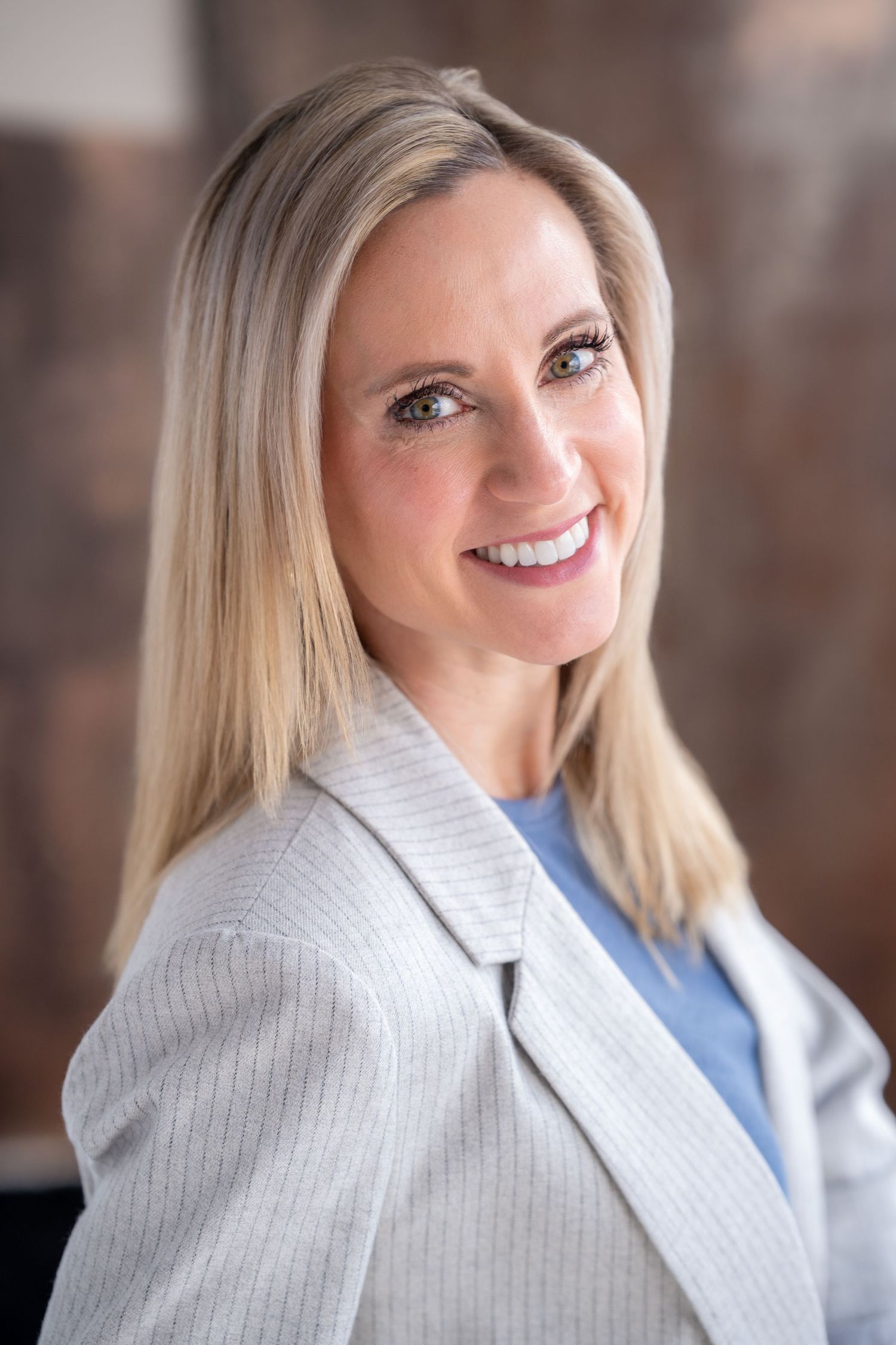 Blonde woman in gray blazer smiling confidently in professional headshot.
