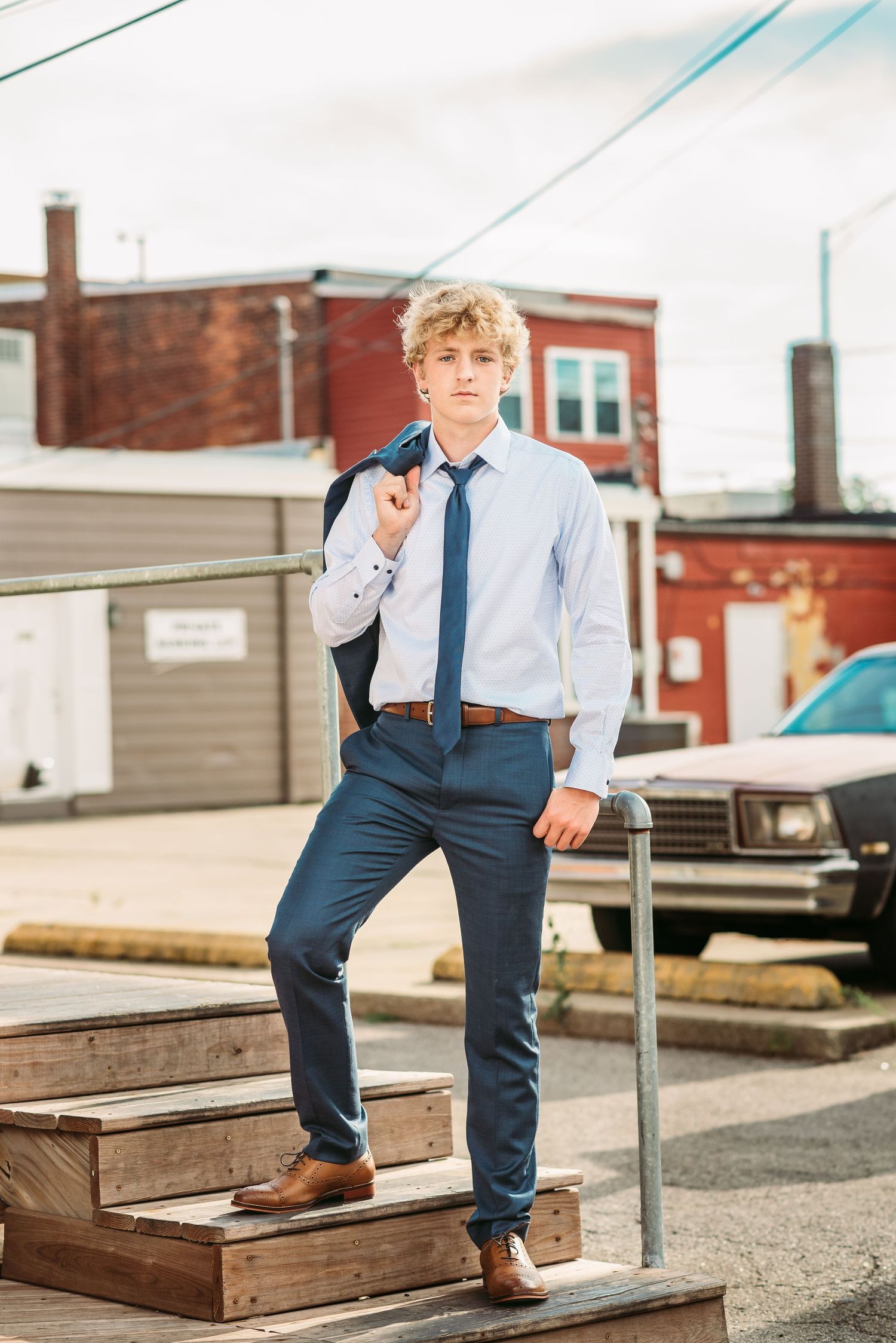 Stylish young man in blue dress shirt and tie posing on wooden steps in urban setting.