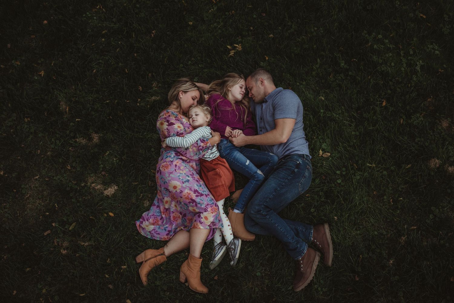 Family of four lying together on grass in a cozy overhead portrait shot.