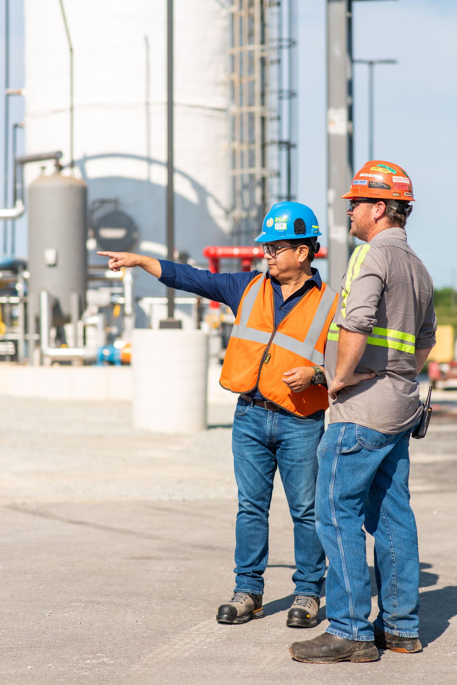 Two construction workers in hard hats and safety vests inspecting industrial facility.