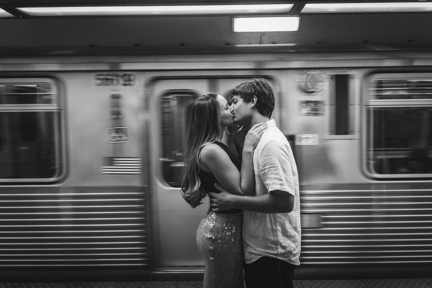 Romantic black and white couple kissing on subway platform with blurred moving train.