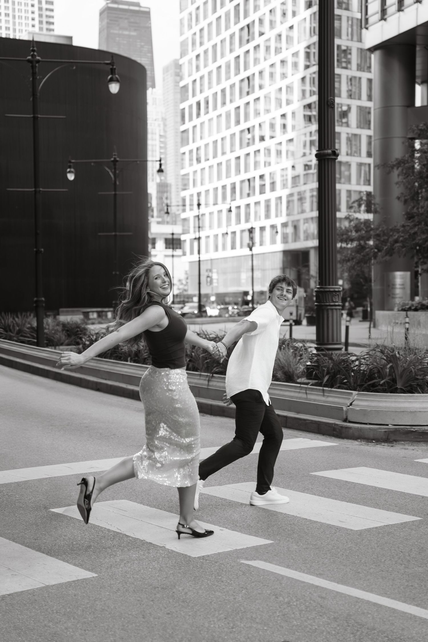 A cheerful couple dances playfully on a city crosswalk in black and white photo.