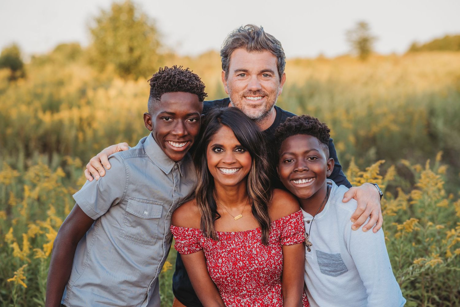 Diverse family of four smiling together in a golden field during sunset.