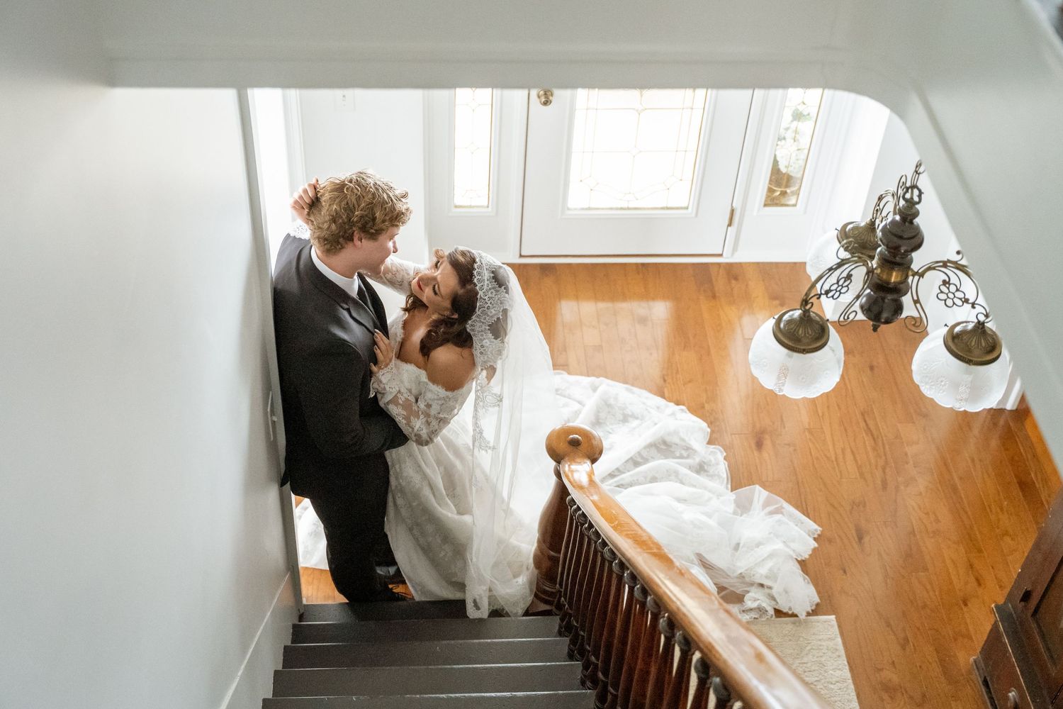 Bride and groom sharing a romantic kiss on a staircase, with wedding dress train draped on wooden steps.