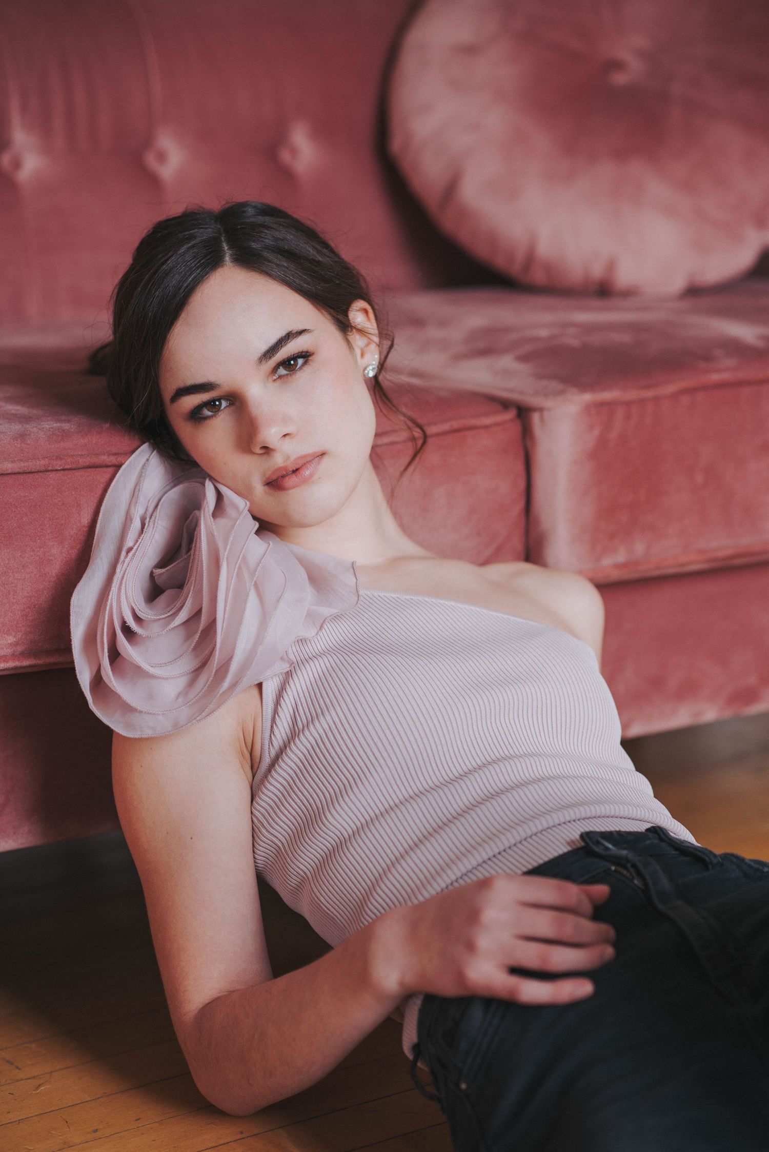 Young brunette woman in pink off-shoulder top relaxes against a velvet blush sofa.