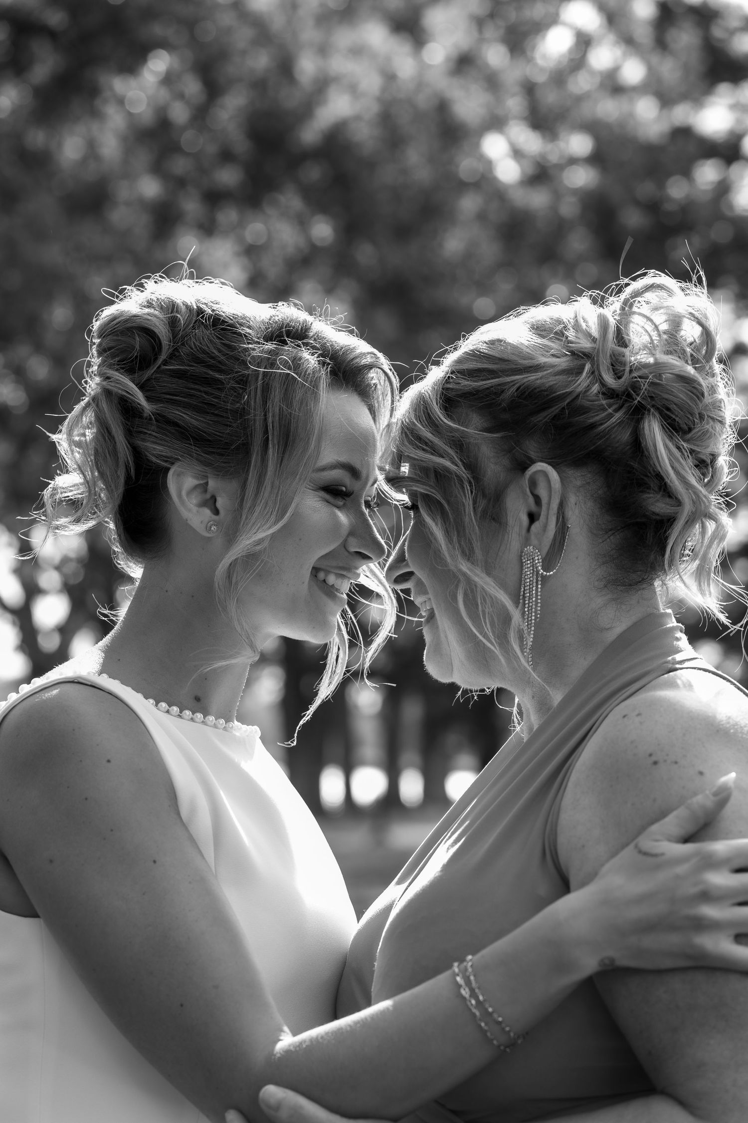 Black and white photo of two brides embracing and smiling at each other outdoors on their wedding day.