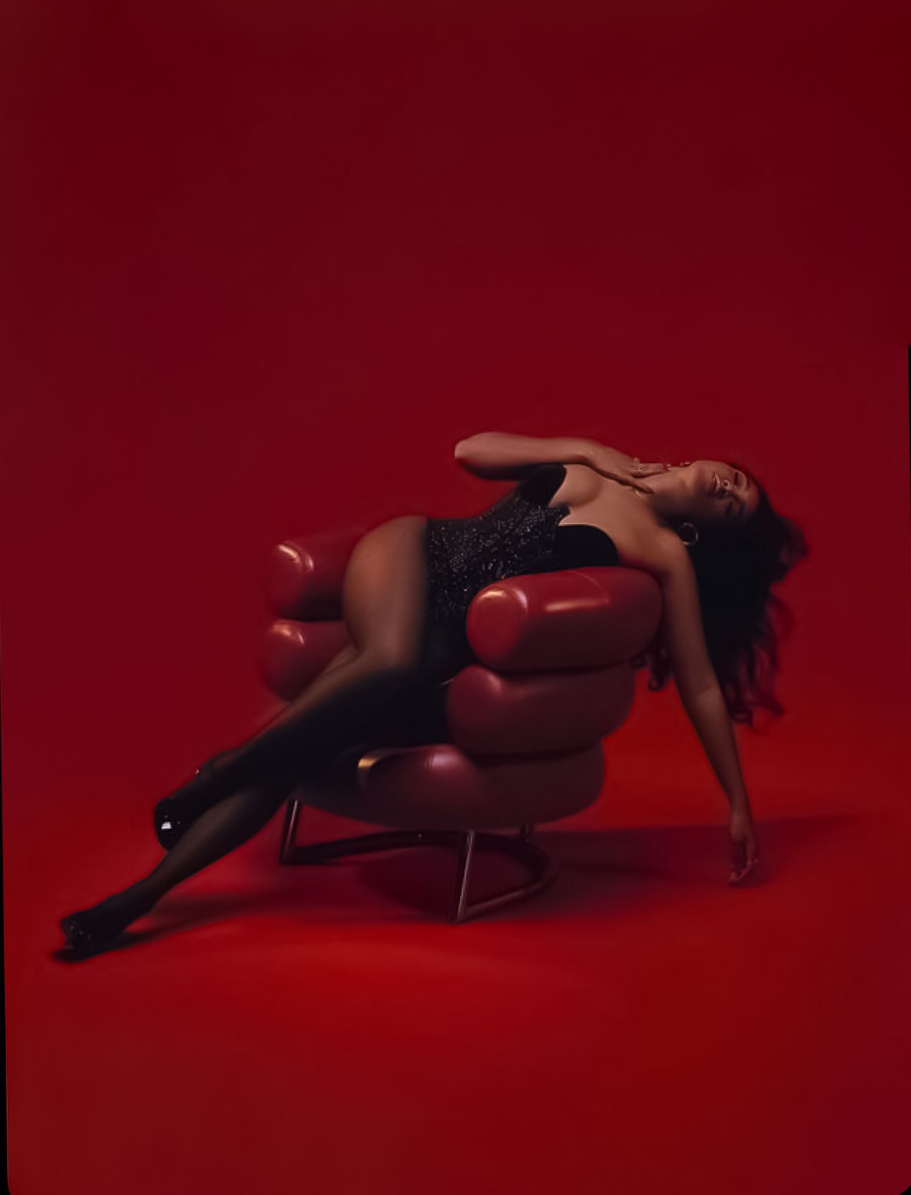Artistic boudoir photo with red background showing figure reclining on modern curved lounge chair.