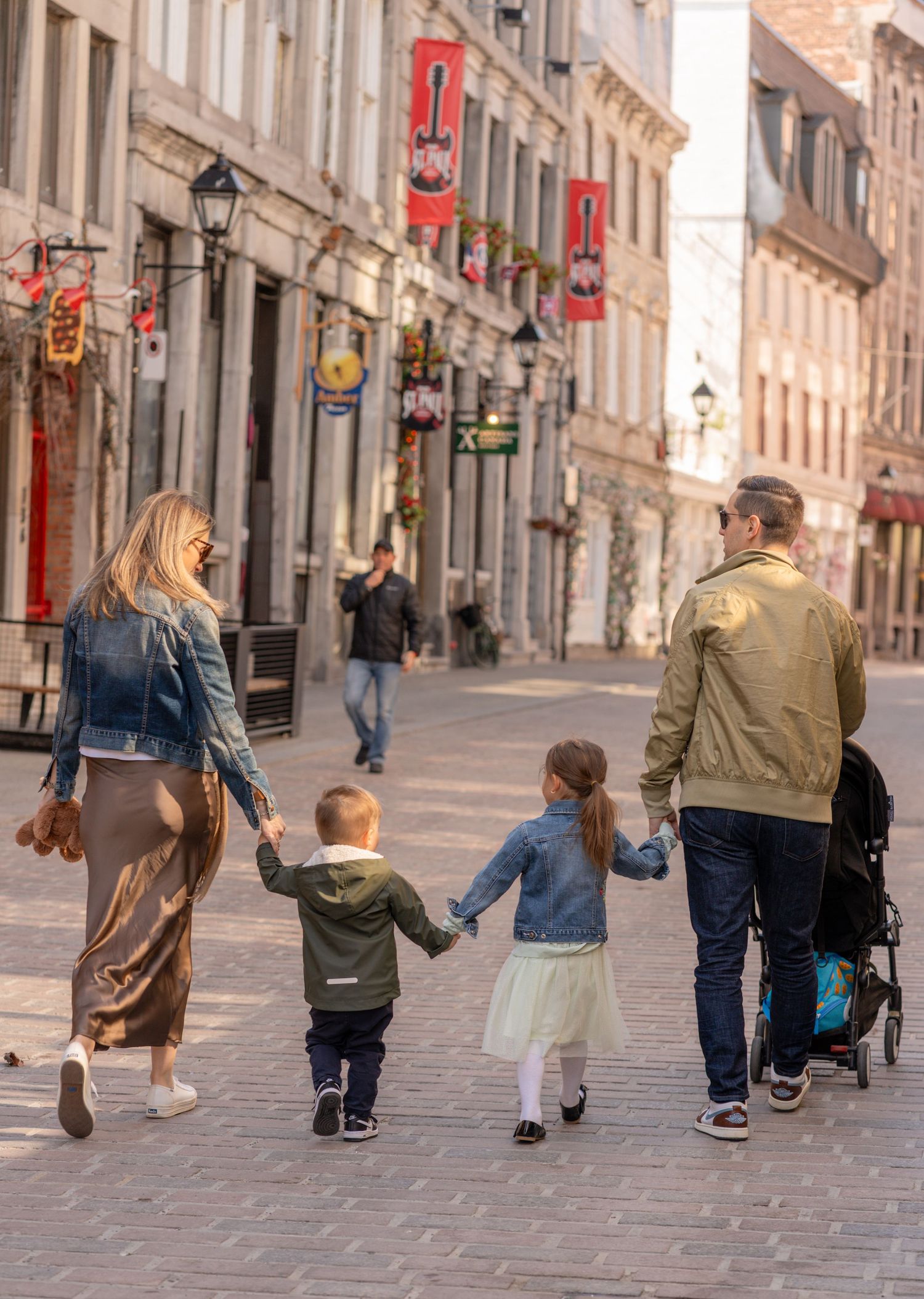 Family of four walking hand-in-hand down a charming cobblestone street in Old Montreal, Quebec, Canada.