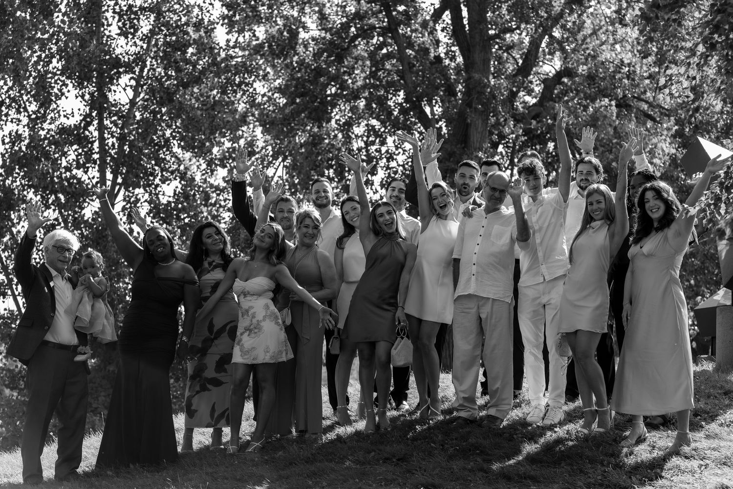 Black and white photo of a large group of people standing outdoors under trees, raising their arms in celebration.