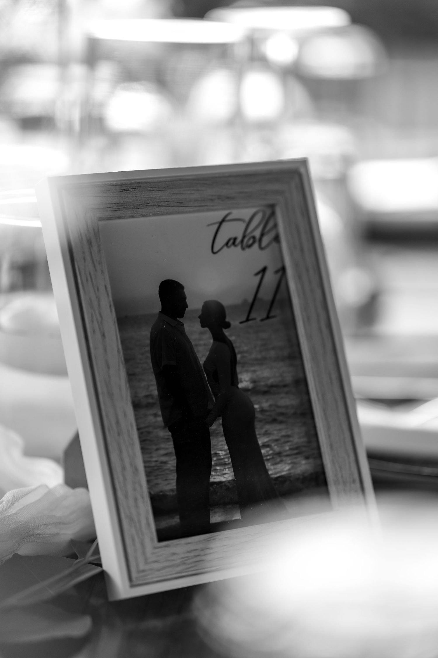 Black and white framed photo of couple silhouetted by ocean used as wedding table number 11 card.